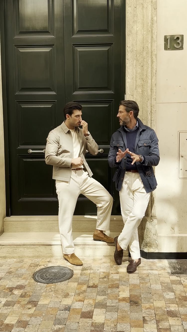 Two men dressed in elevated casual attire standing outside a large black door.