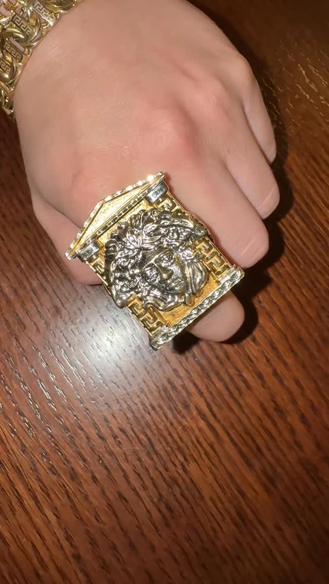 A hand wearing a large, decorative gold and silver Medusa-style ring on a wooden table.