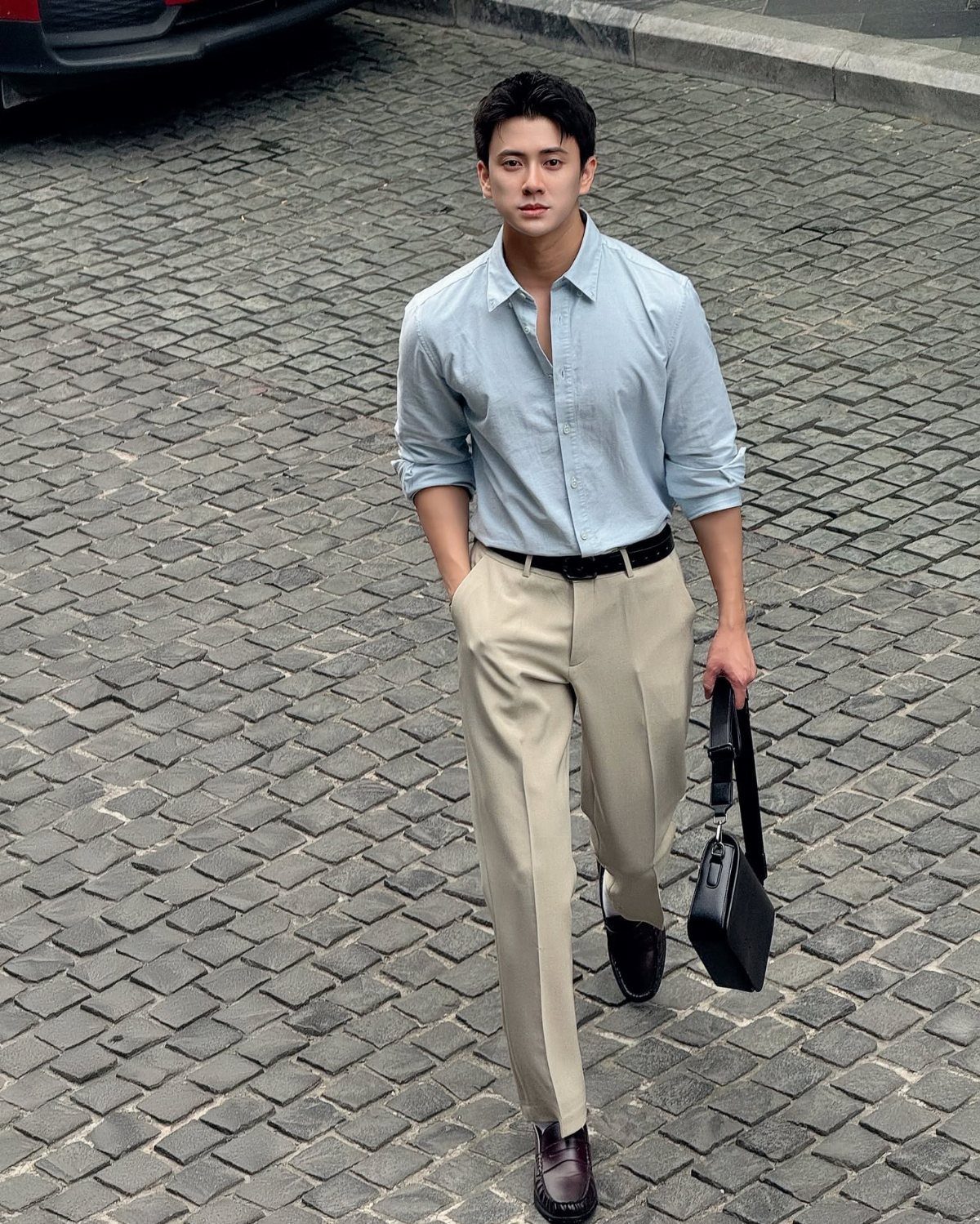 Man in light blue shirt and beige dress pants walking on a cobblestone street.