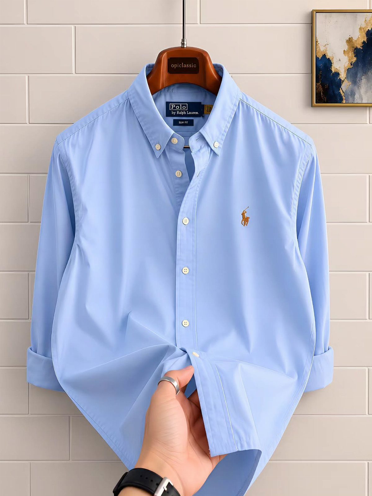 Light blue button-down shirt with a small embroidered logo hanging on a wooden hanger.