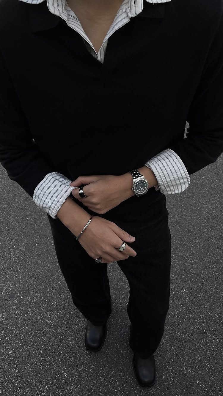 Man wearing a black long-sleeved knit polo shirt with striped cuffs and black trousers.