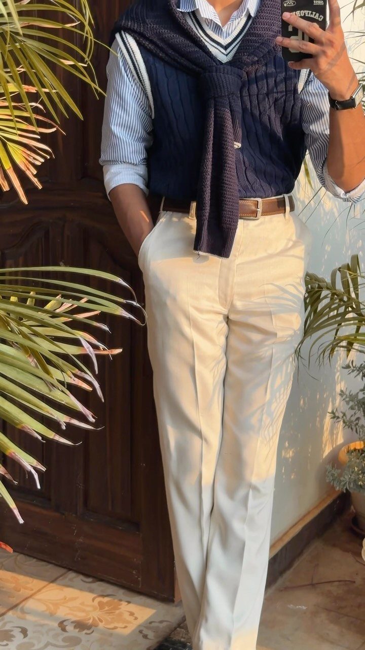 Man in white tailored trousers, striped shirt, and navy sweater draped over shoulders.