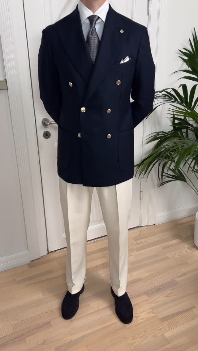 A man wearing a navy double-breasted blazer with gold buttons and cream trousers.
