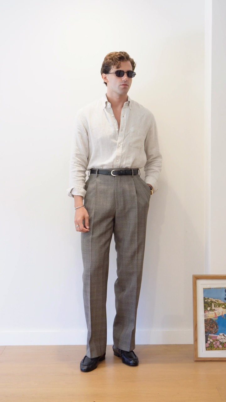 A man wearing a linen shirt and grey plaid tailored trousers with black loafers.