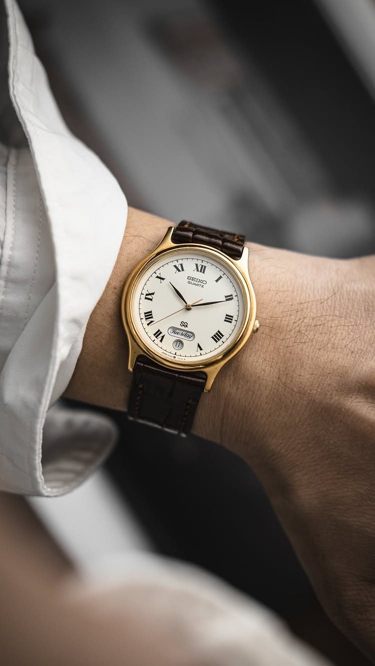 A gold wristwatch with a white face and brown leather strap on a person's wrist.