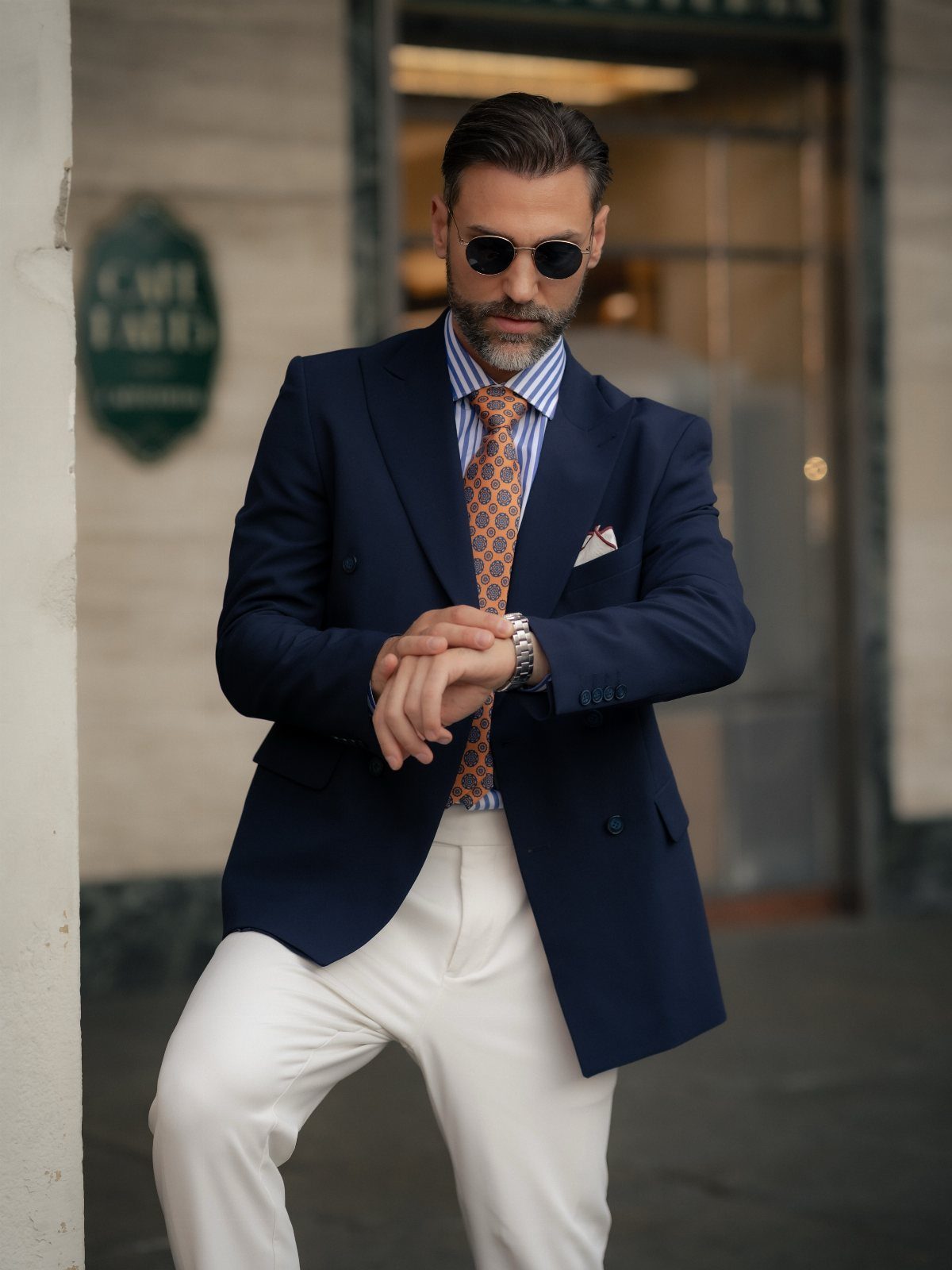 Man in a navy blue blazer, striped shirt, and patterned tie posing outdoors.