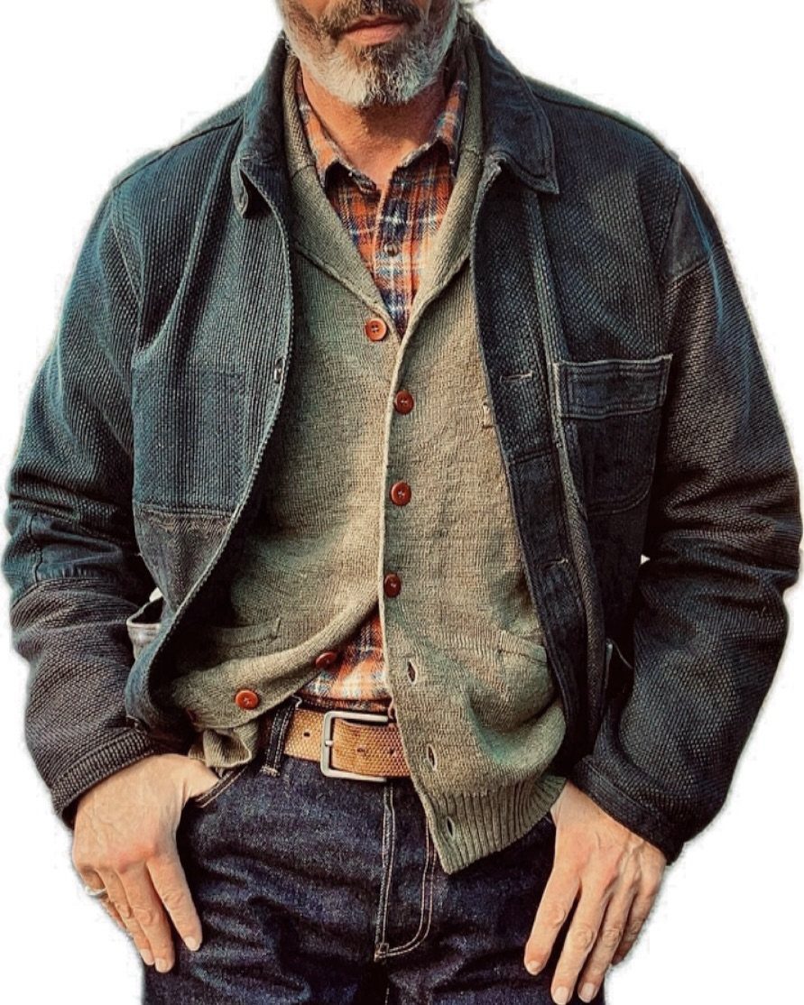 An older man wearing a dark blue casual jacket, green cardigan, and plaid shirt.