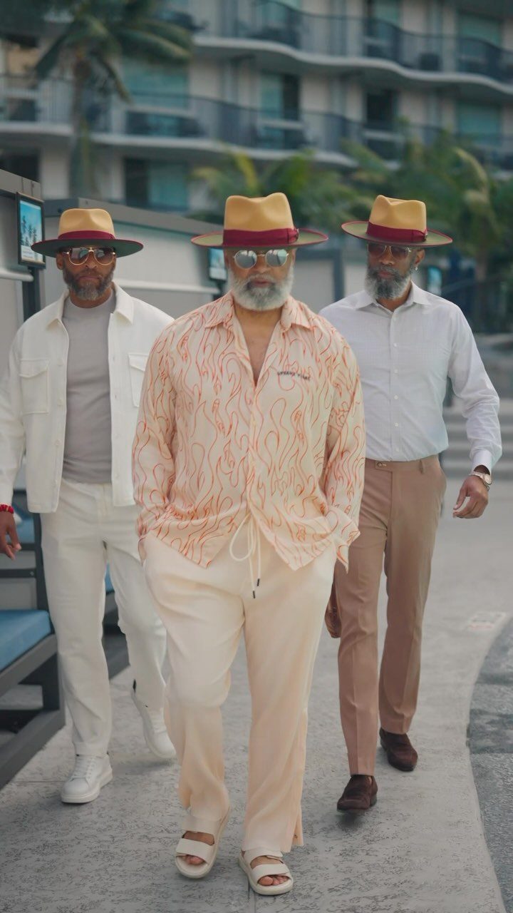 Three stylish older men walking together wearing summer outfits and straw fedora hats.