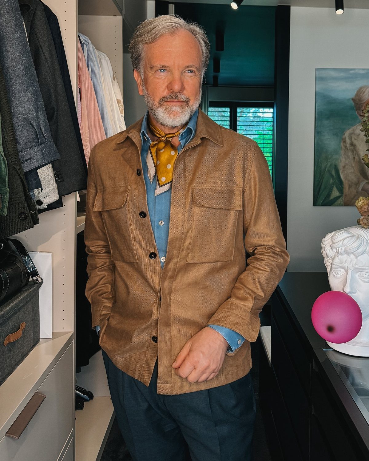 An older man with grey hair posing in a stylish brown jacket and blue shirt.