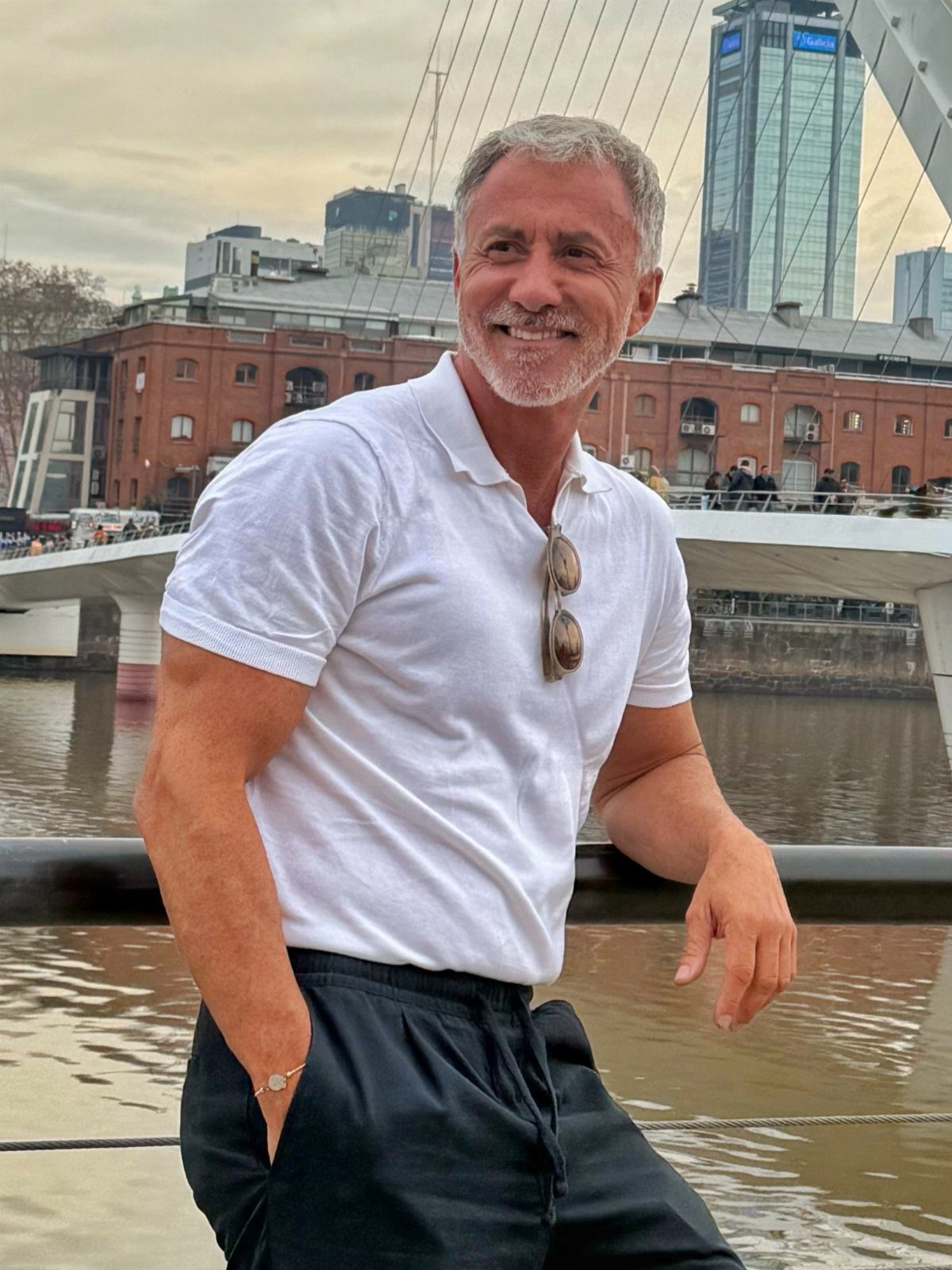A smiling older man with grey hair wearing a white polo shirt outdoors.