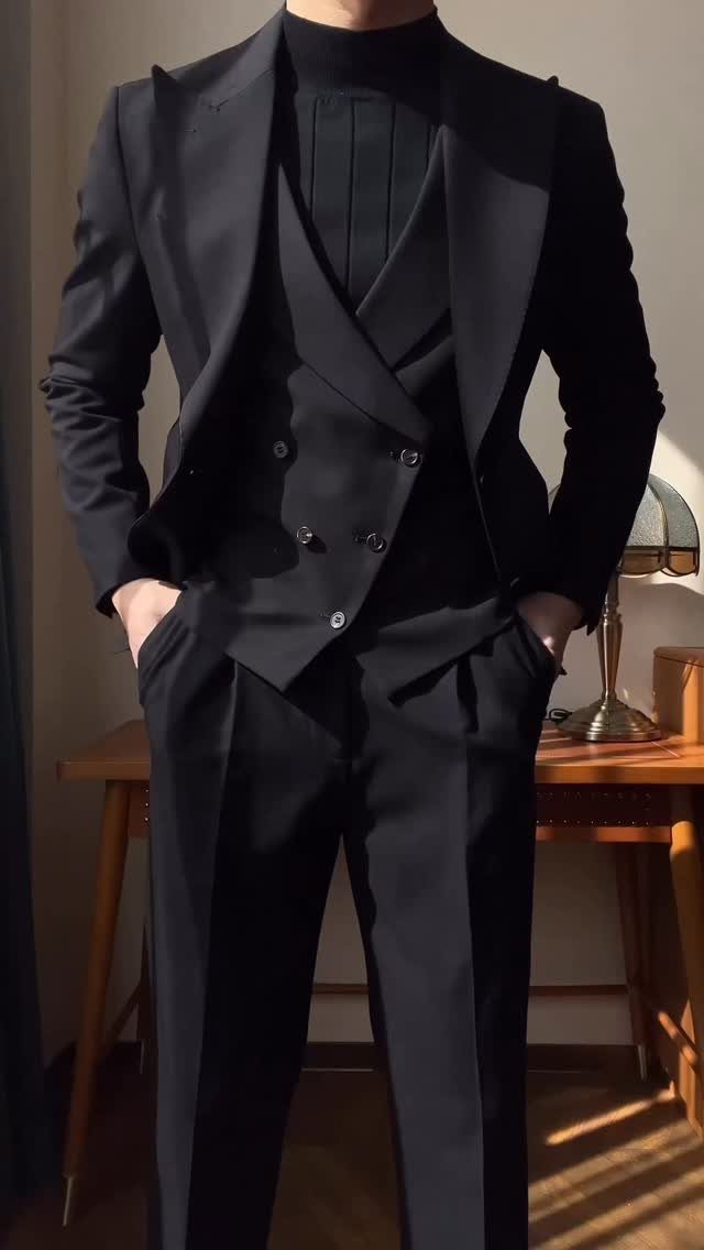 A person wearing a dark three-piece tailored suit and a black turtleneck sweater.