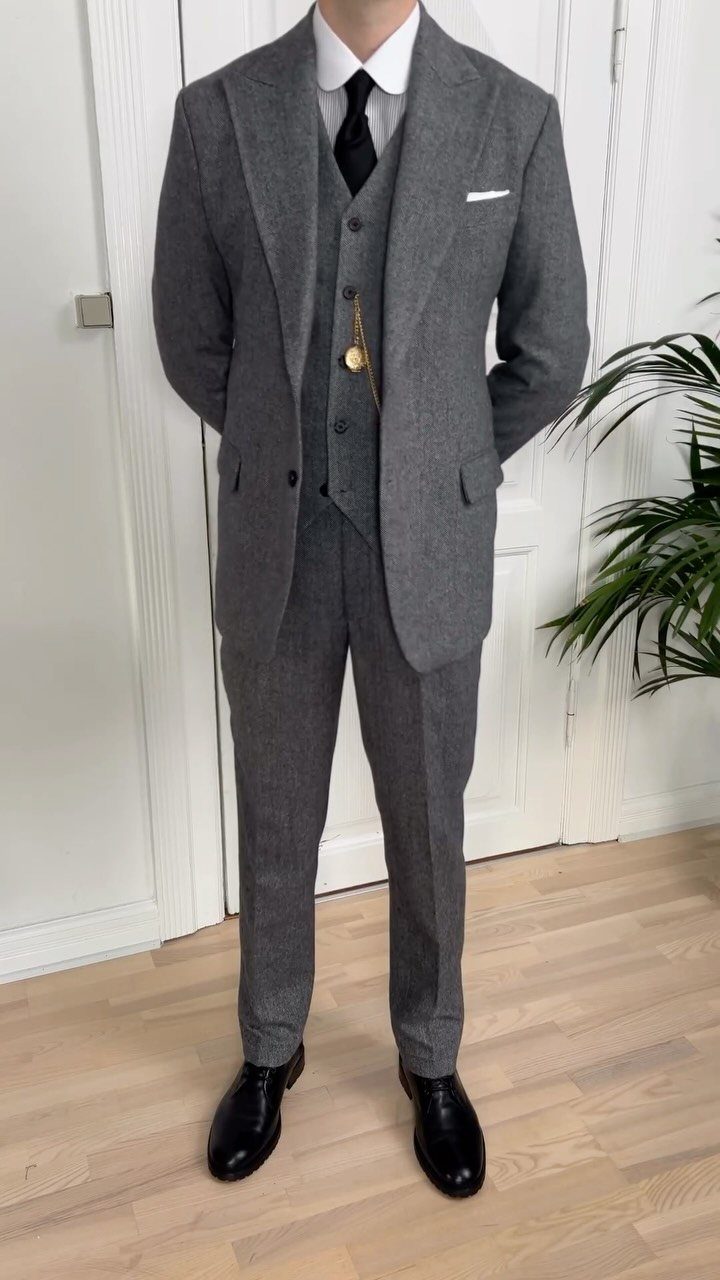 A person standing in a grey three-piece tweed suit with a pocket watch chain.