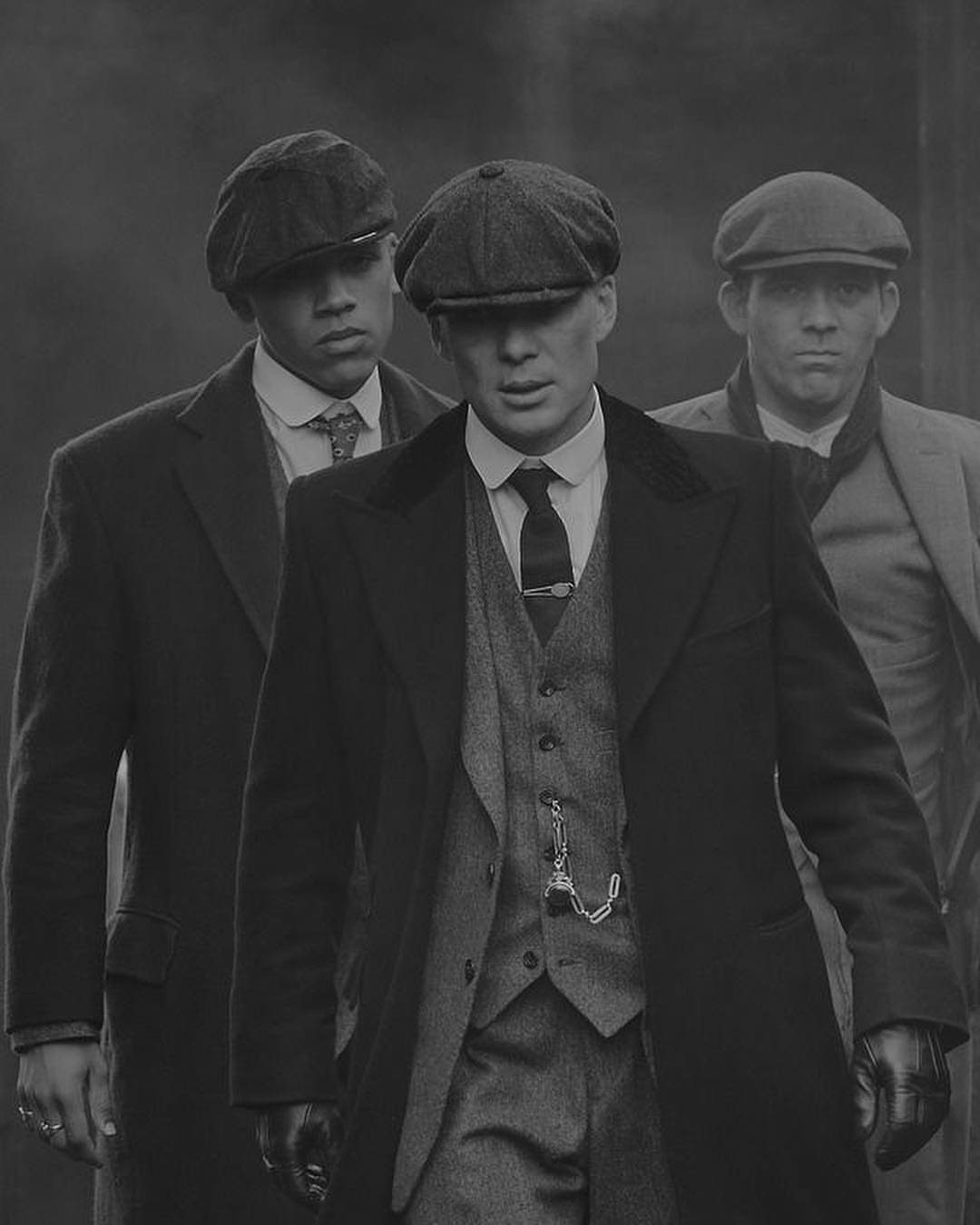 Three men dressed in vintage 1920s style three-piece suits and newsboy caps standing outdoors.