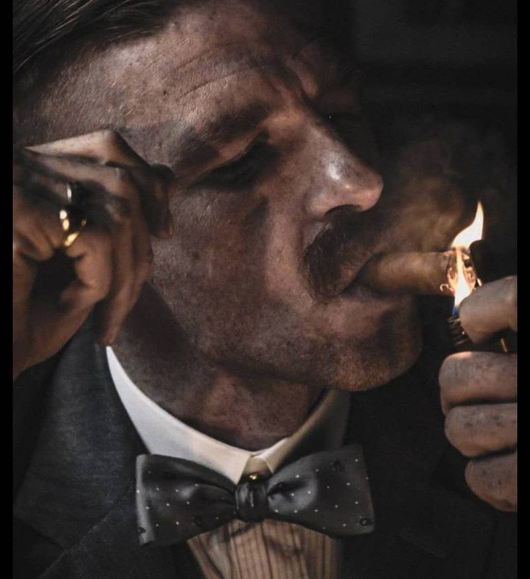 A man with a mustache lighting a cigar while wearing a dark suit and bow tie.