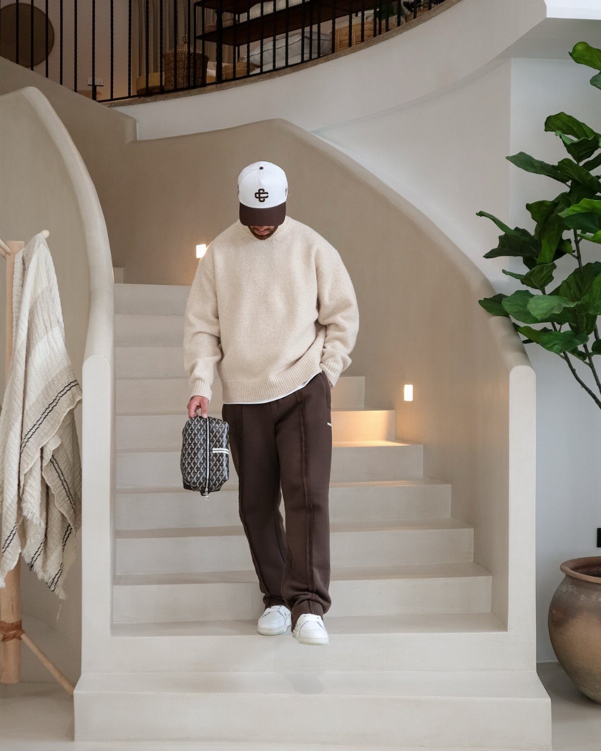 Man in cream knit sweater and brown sweatpants walking down minimalist stairs.