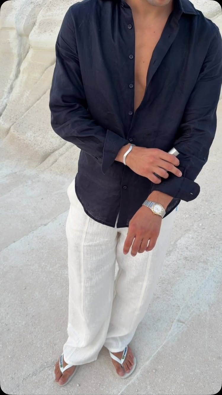 Man wearing a dark navy button-down shirt and white linen trousers standing outdoors.
