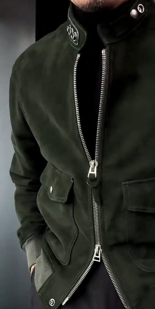 A man wearing a dark olive green suede jacket and a black turtleneck sweater.