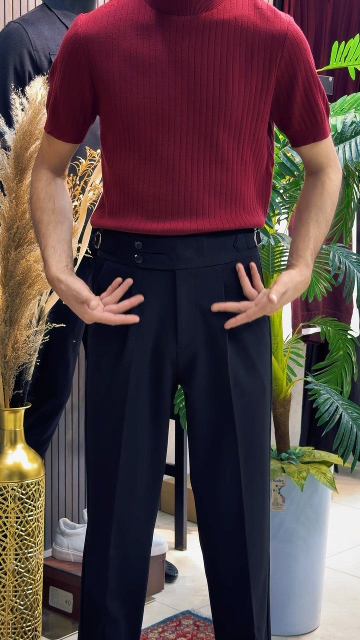 Man wearing a maroon ribbed shirt tucked into black high-waisted trousers.
