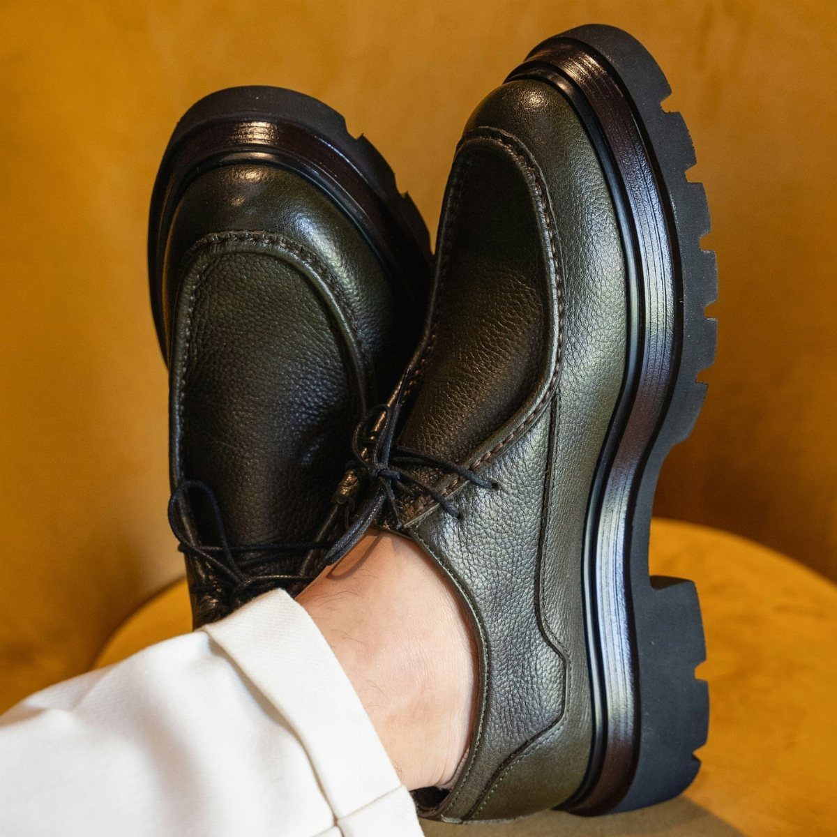 Dark metallic leather derby shoes with thick black lug soles worn with white trousers.