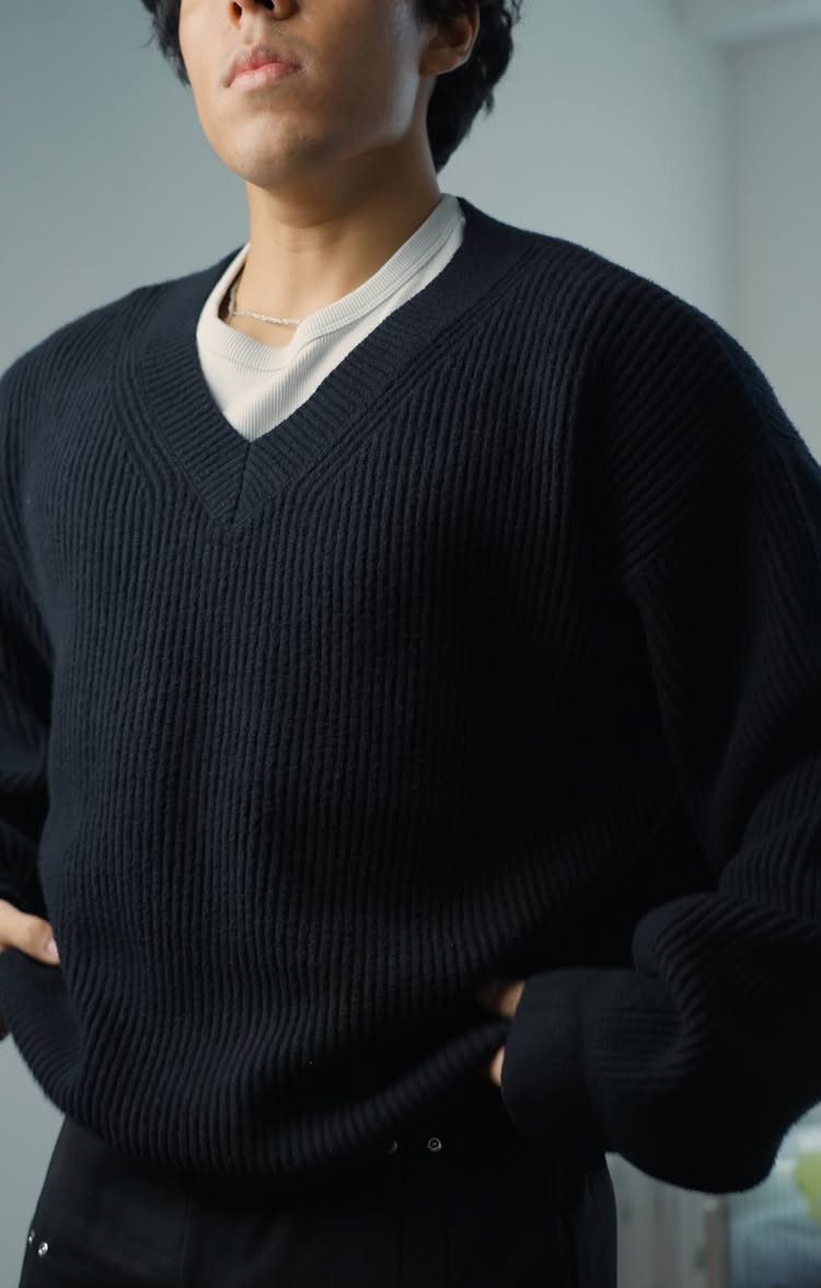A man wearing a black ribbed V-neck sweater over a white shirt.