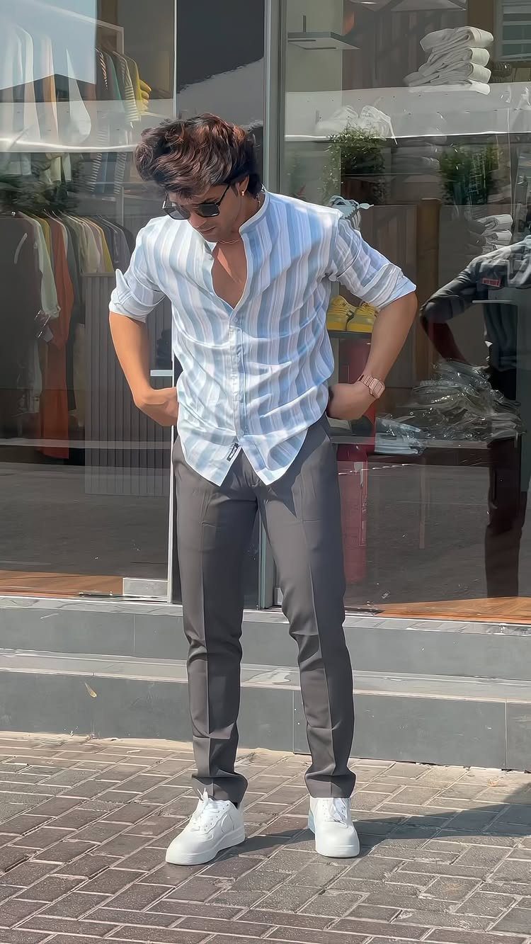 Man in a striped short-sleeved shirt and grey trousers posing in front of a shop.
