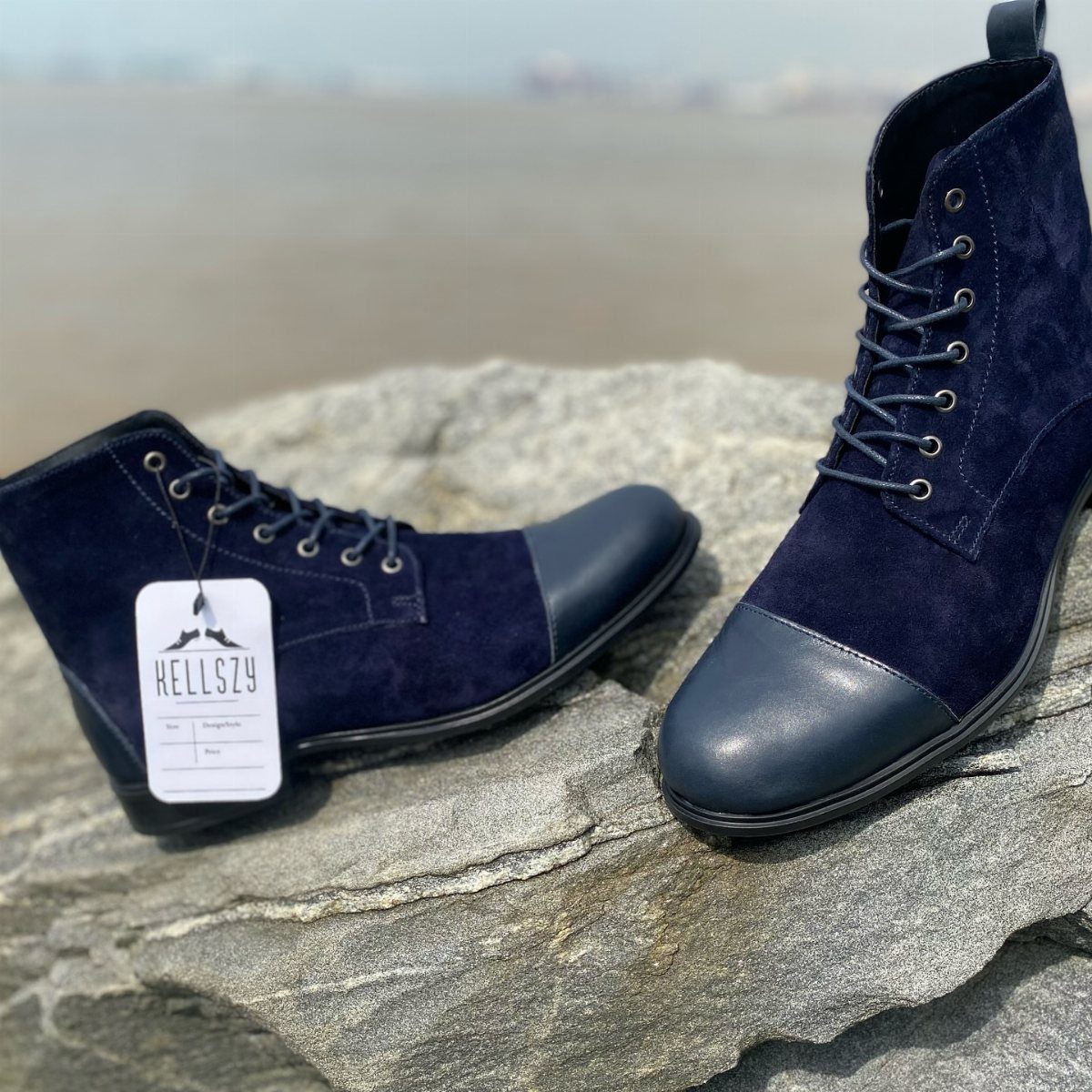 Navy blue suede lace-up ankle boots with leather toe caps resting on a large grey rock.