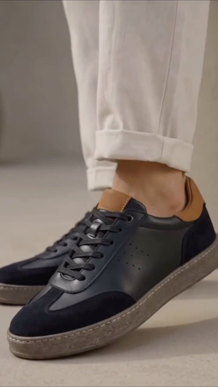 Navy blue leather and suede sneakers worn with light beige cuffed chino trousers.