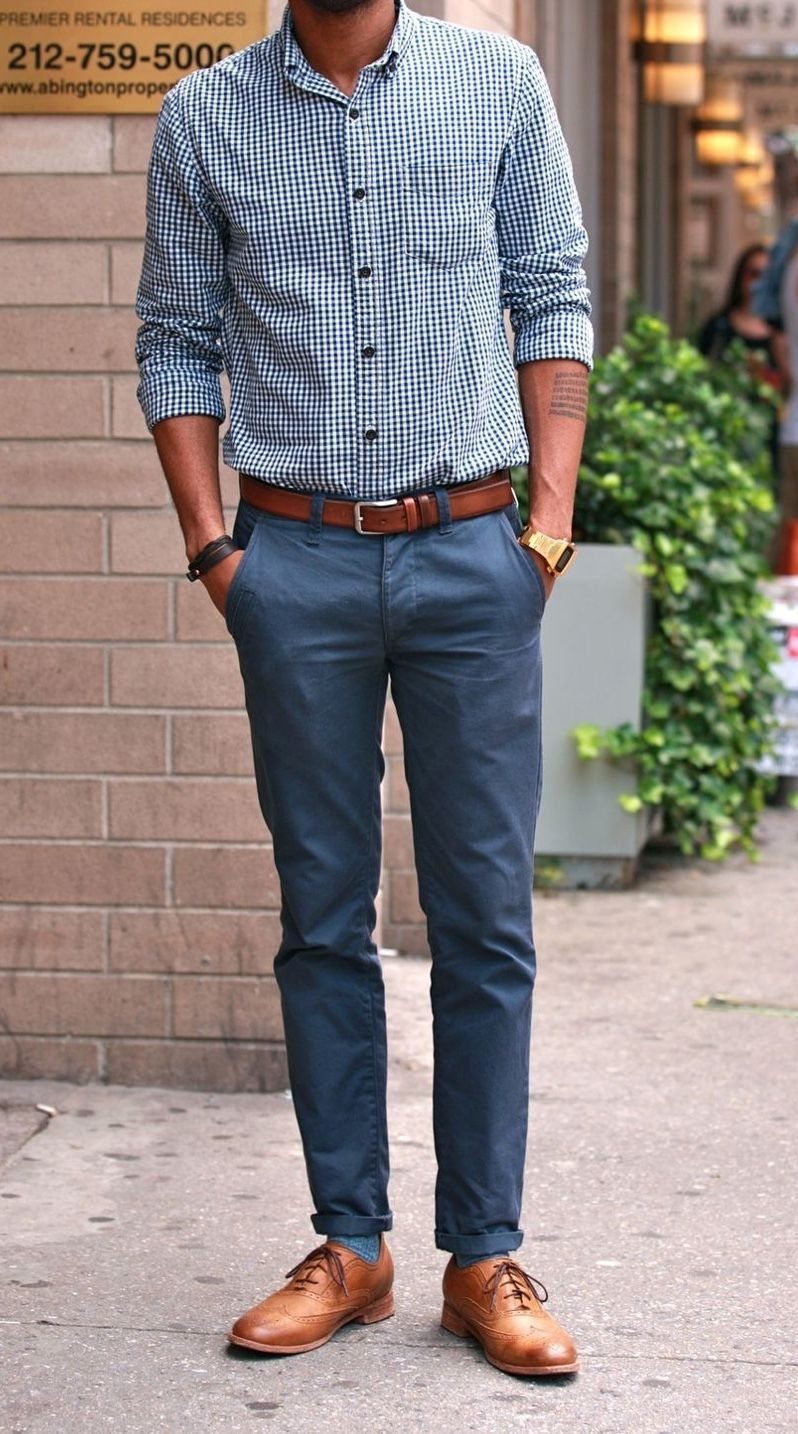 Man wearing a checkered shirt, blue trousers, and tan leather shoes standing on a sidewalk.