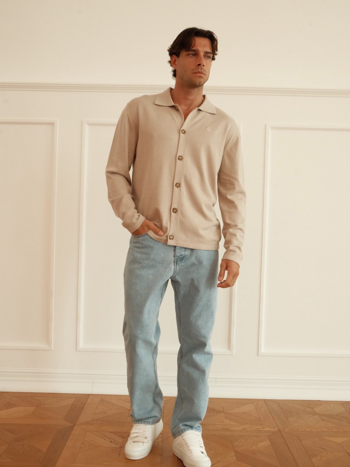 Man wearing a beige button-down lightweight knit sweater and light blue jeans.