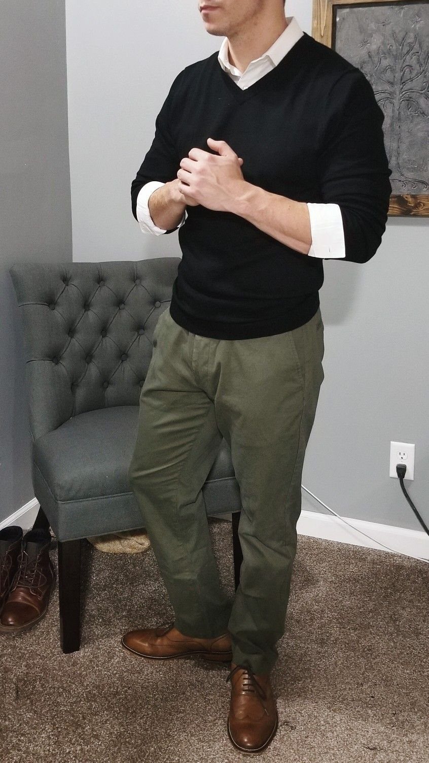 Man wearing a black sweater, white shirt, and olive green pants with brown shoes.