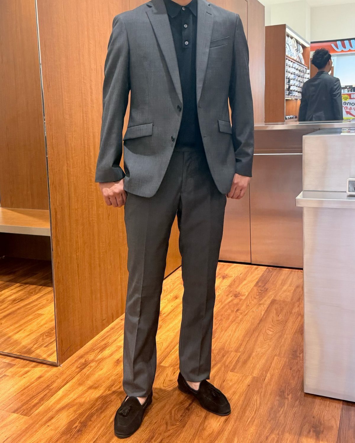 A person wearing a dark polo shirt paired with a dark gray suit and black loafers.