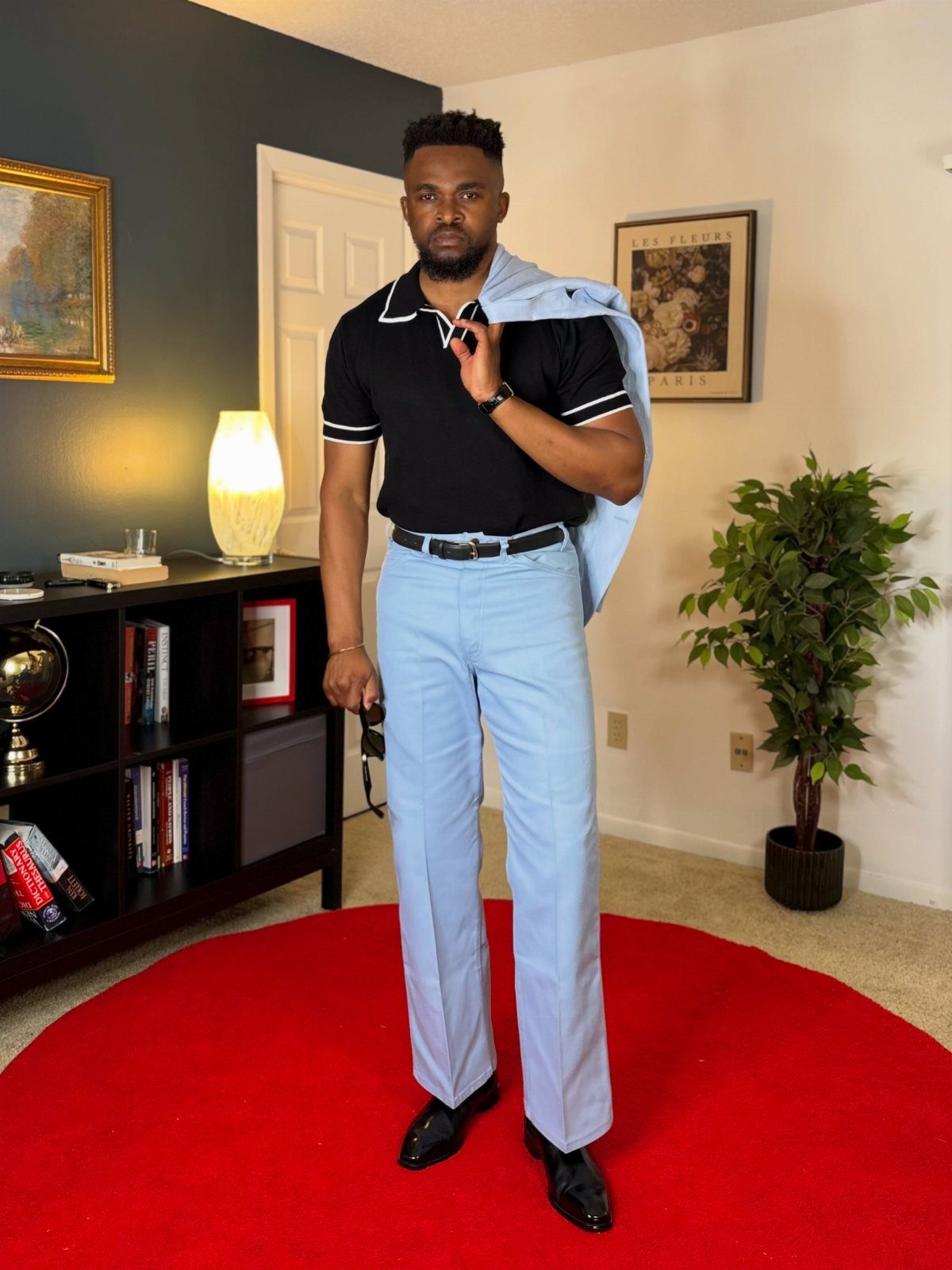 Man wearing a black polo shirt and light blue trousers holding a matching suit jacket.
