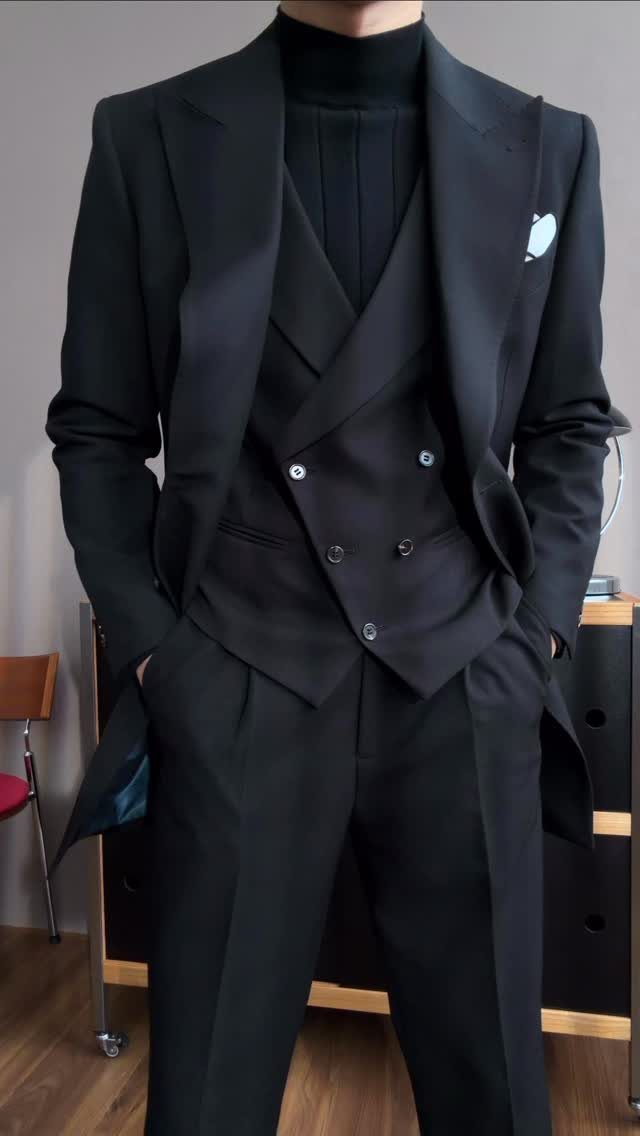 Man wearing a black three-piece suit with a black turtleneck sweater and white pocket square.