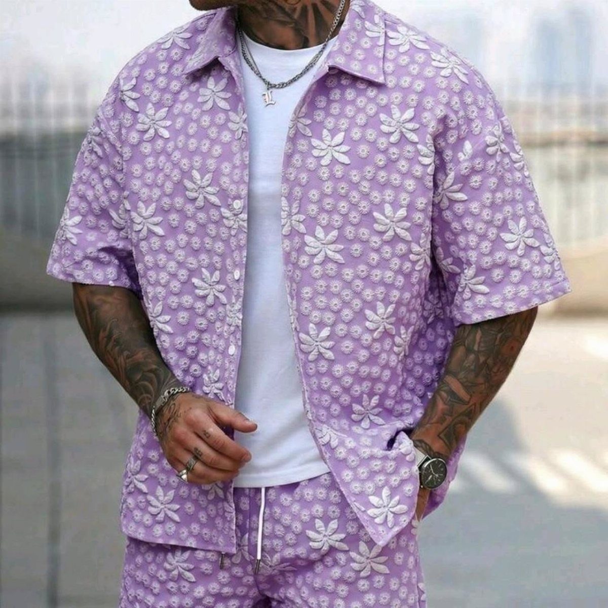 Man wearing a light purple floral patterned short-sleeved shirt and matching shorts set.