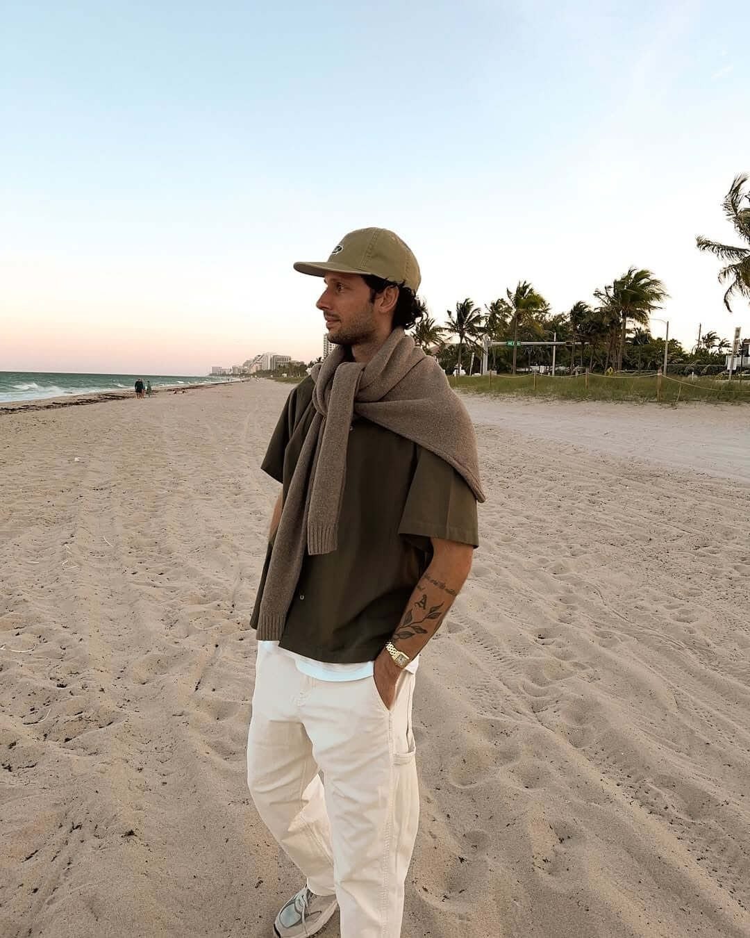 A man wearing white pants and an olive shirt standing on a sandy beach.