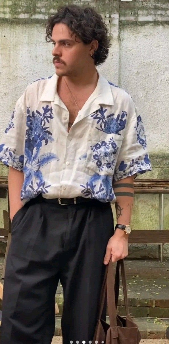 A man wearing a blue floral short-sleeved shirt and black trousers standing outdoors.