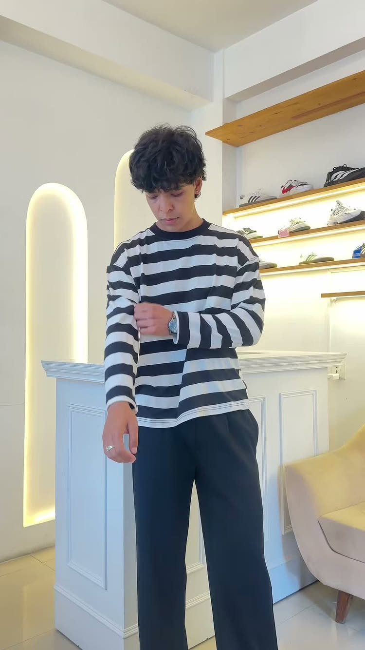 A young man wearing a black and white horizontally striped long-sleeved shirt and dark pants.