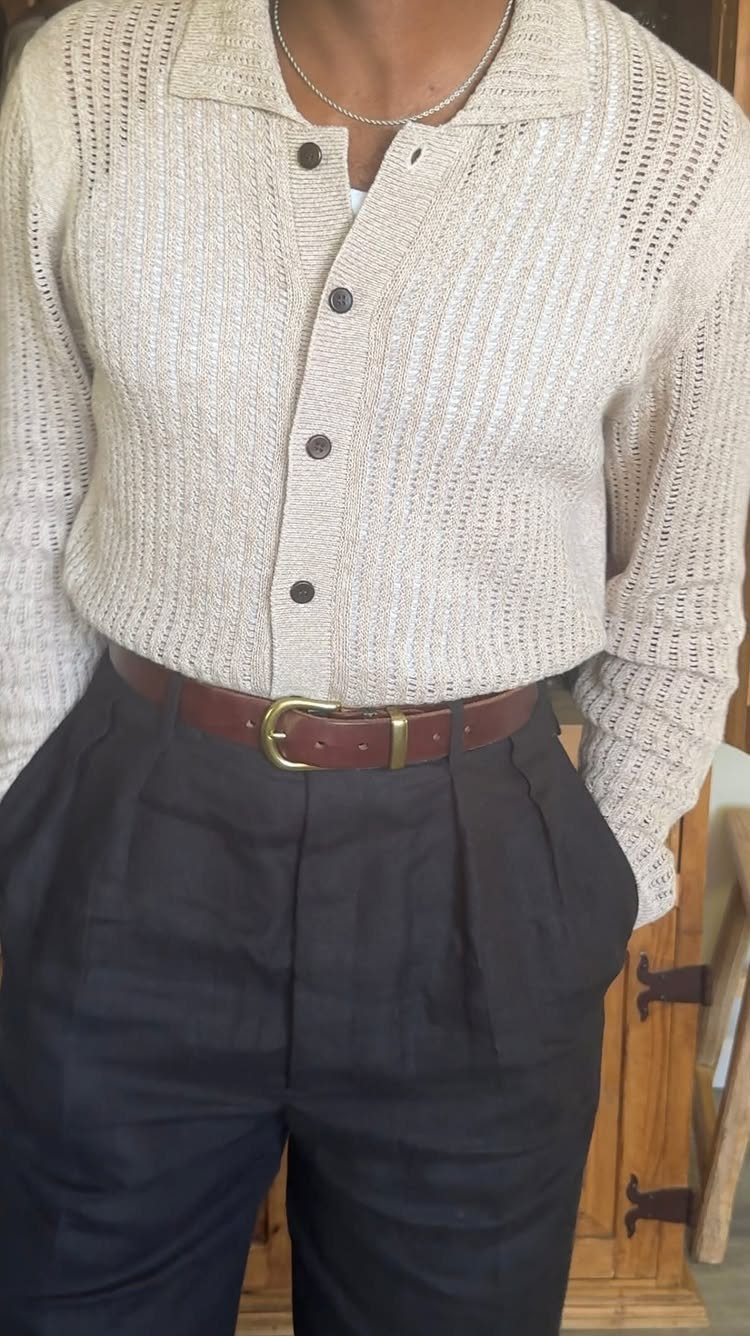 Person wearing a cream knit cardigan, dark navy pleated trousers, and a brown leather belt.