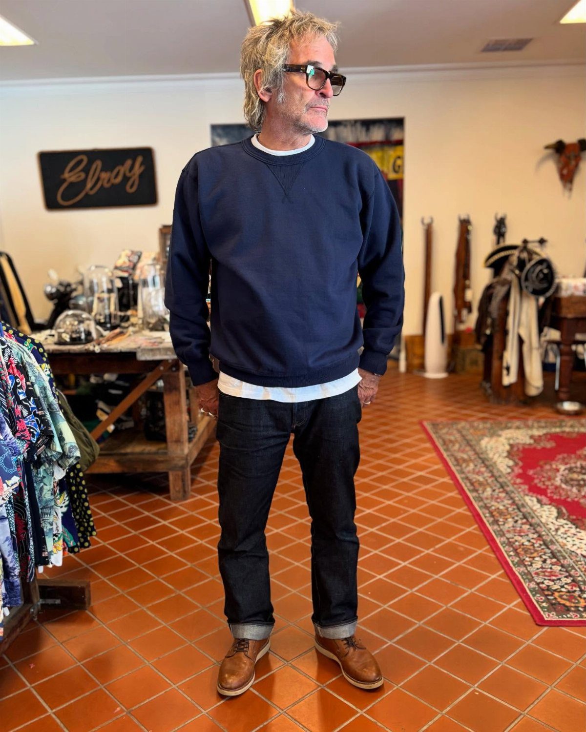 Man wearing a navy blue crew neck sweatshirt, dark jeans, and brown leather shoes.