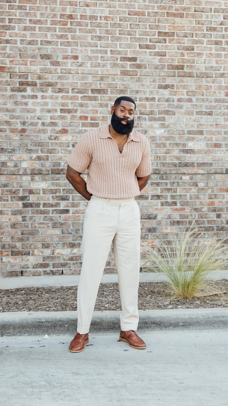 A bearded man in a beige knit polo and cream trousers wearing brown leather dress shoes.
