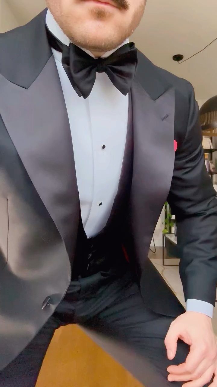 A man dressed in a formal black tuxedo with a bow tie and pink pocket square.