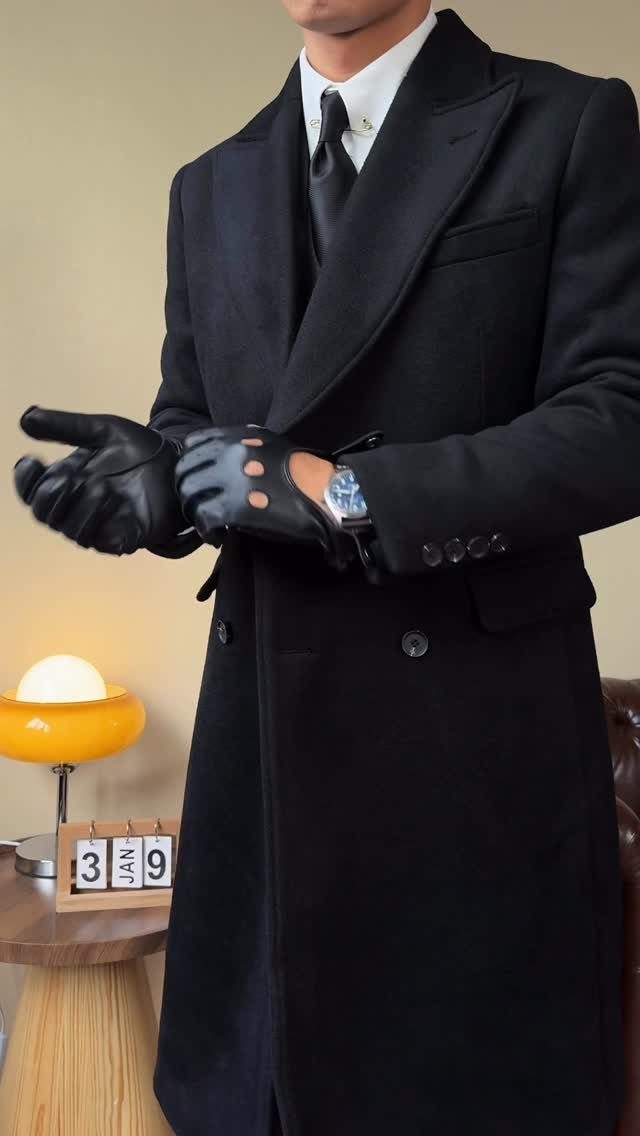 A man dressed in a formal black overcoat, white shirt, tie, and black leather gloves.