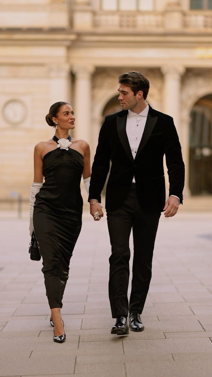 A man in a black velvet tuxedo and a woman in a black satin dress walking together.