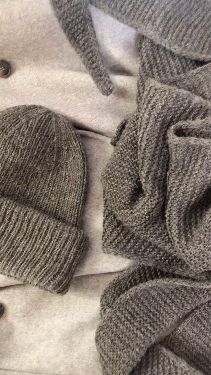 Grey knit beanie, textured scarf, and a light grey coat laid out together.