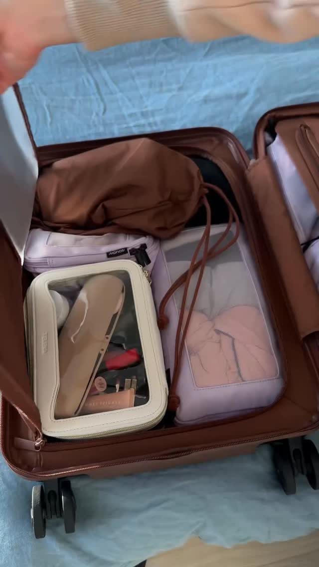 An open brown suitcase filled with various organized packing cubes and travel accessories.