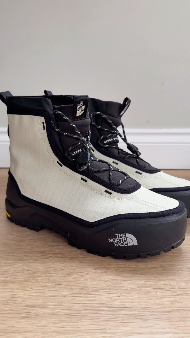 Cream and black The North Face waterproof boots resting on a wooden floor.