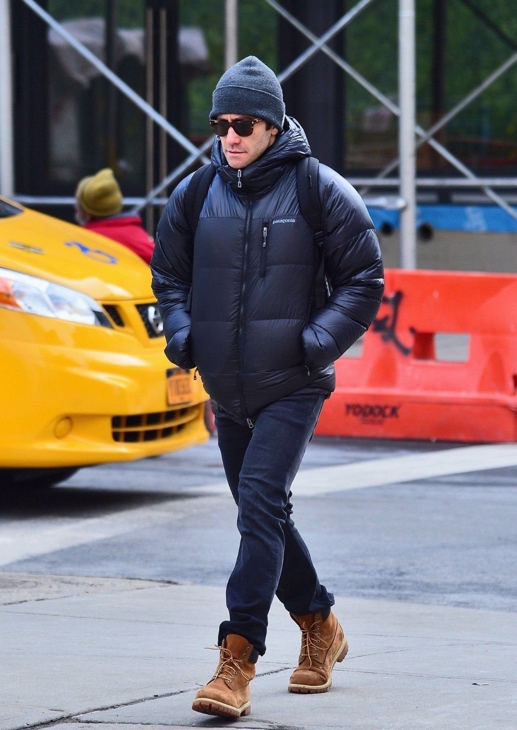 A man walking in a city wearing a black puffer jacket, beanie, and tan boots.